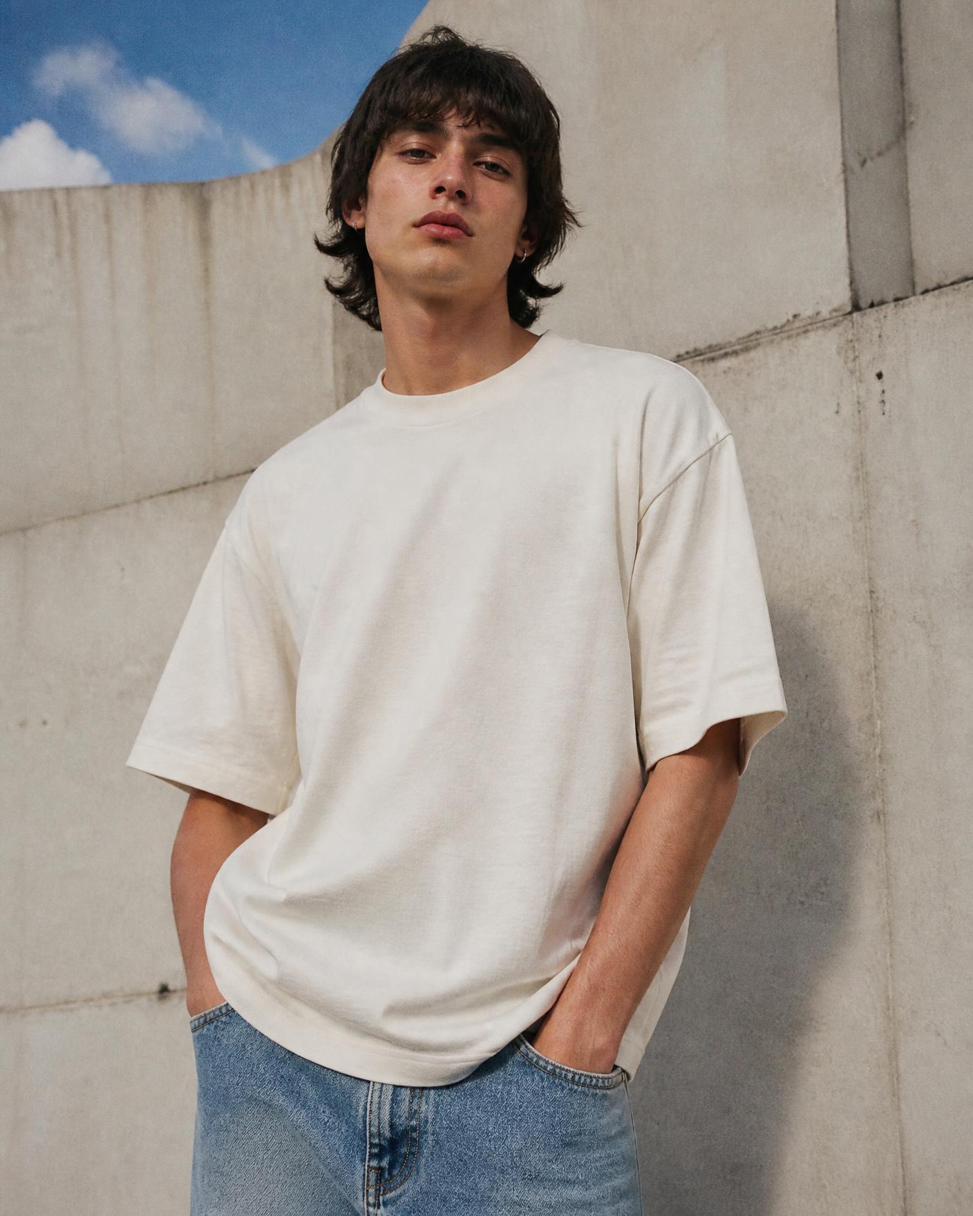 Model in an off-white boxy Atelier Corner t-shirt against a concrete wall